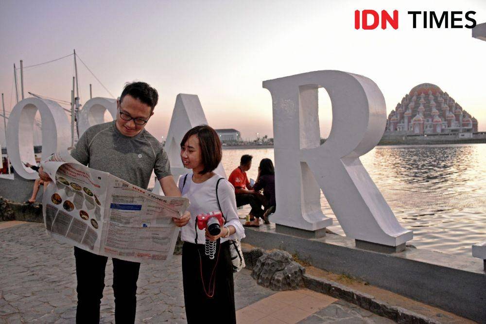 Dua orang tengah membaca koran IDN Times dengan latar belakang foto Masjid 99 Kubah di CPI Makassar/Irwan Idris