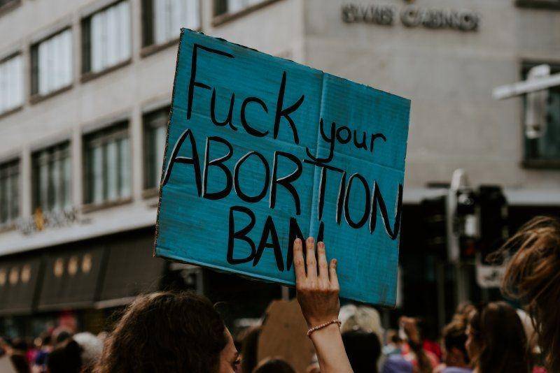 Ilustrasi seorang demonstran perempuan membawa poster yang berarti "Persetan dengan Larangan Aborsimu". unsplash.com/Claudio Schwarz
