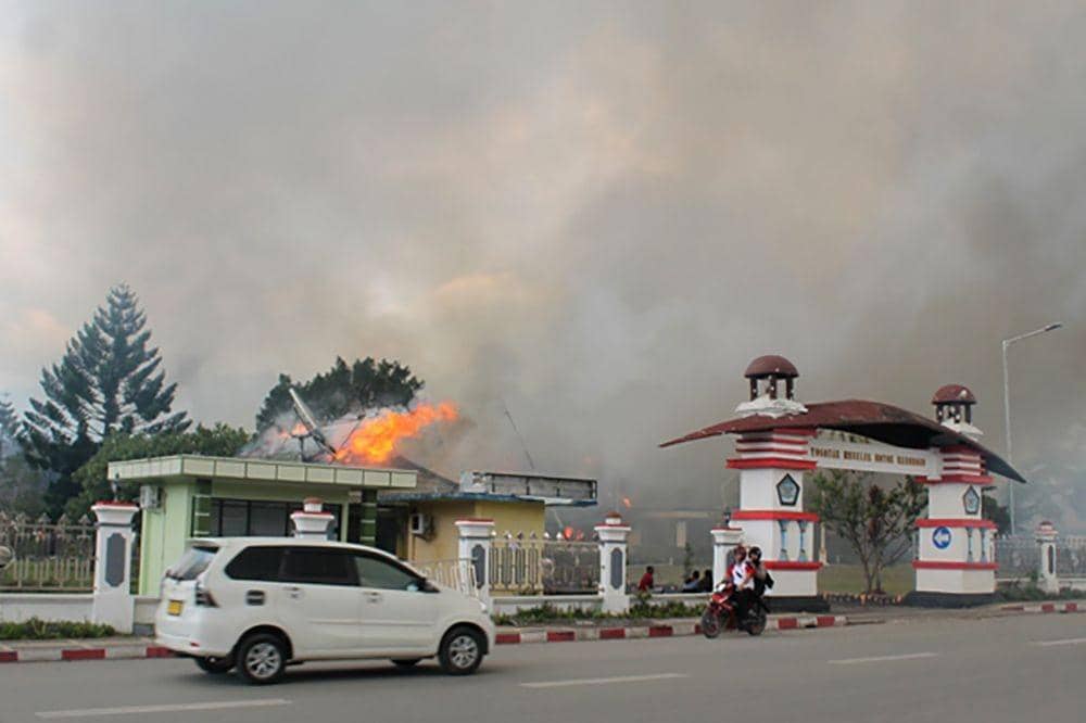 Pengendara melintasi kantor Bupati Jayawijaya yang terbakar saat aksi unjuk rasa di Wamena, Jayawijaya, Papua, pada 23 September 2019. ANTARA FOTO/Marius Wonyewun