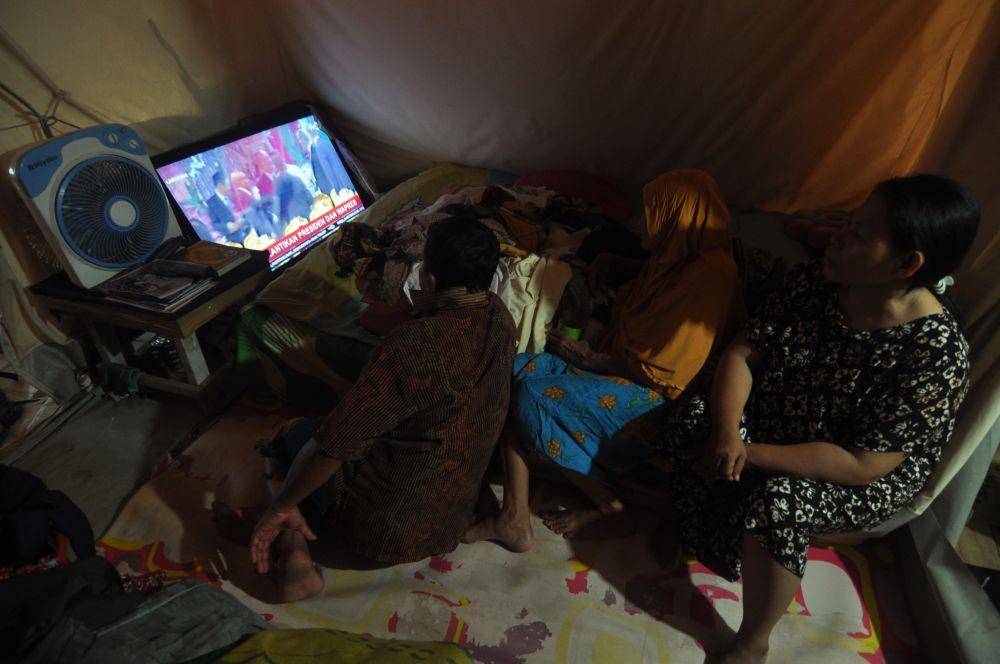 (Warga korban bencana gempa dan likuefaksi menyaksikan siaran langsung pelantikan Presiden dan Wakil Presiden periode 2019-2024 melalui layar televisi di tenda hunian mereka di Kamp Pengungsian Balaroa, Palu, Sulawesi Tengah, Minggu (20/10/2019)) ANTARA FOTO/Mohamad Hamzah