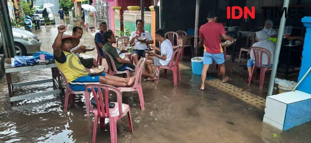 Warga Perum BTP sedang menikmati makanan di atas genangan air. (IDN Times/Hana Adi Perdana)