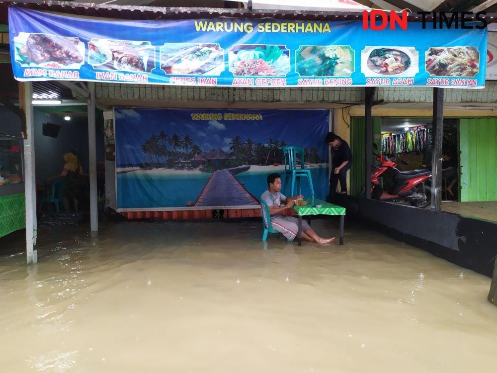 Seorang warga tetap santuy dan asyik saat menikmati makanannya saat banjir di Jalan dr Soetomo Samarinda (IDN Times/Yuda Almerio)