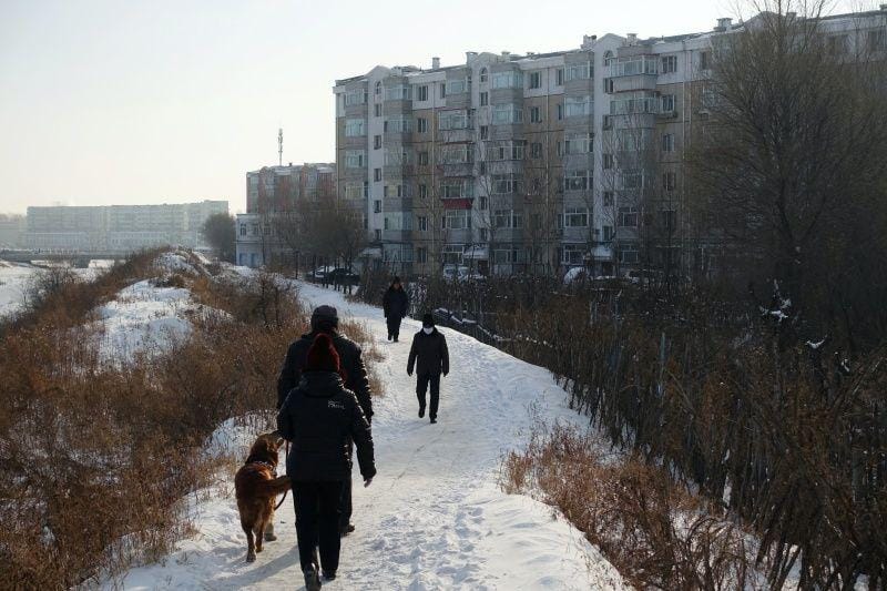Warga berjalan di sebelah gedung tempat tinggal di kota penghasil batubara Hegang, Provinsi Heilongjiang, Tiongkok, pada 2 Januari 2020. Gambar diambil 2 Januari 2020. ANTARA FOTO/REUTERS/Ryan Woo