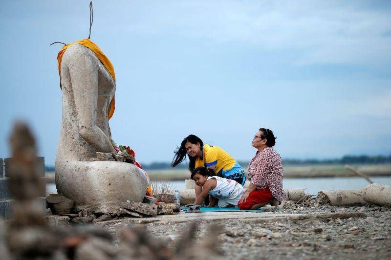 Sebuah keluarga berdoa di dekat reruntuhan patung Budha tanpa kepala, yang muncul di bendungan yang mengering akibat kekeringan, di Lopburi, Thailand, pada 1 Agustus 2019. ANTARA FOTO/REUTERS/Soe Zeya Tun/File Photo