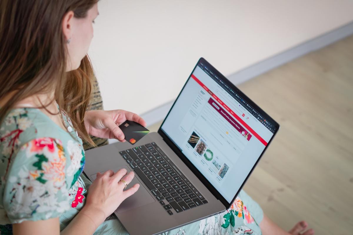 Seseorang berbelanja di situs e-commerce menggunakan laptop dan kartu pembayaran untuk transaksi online.